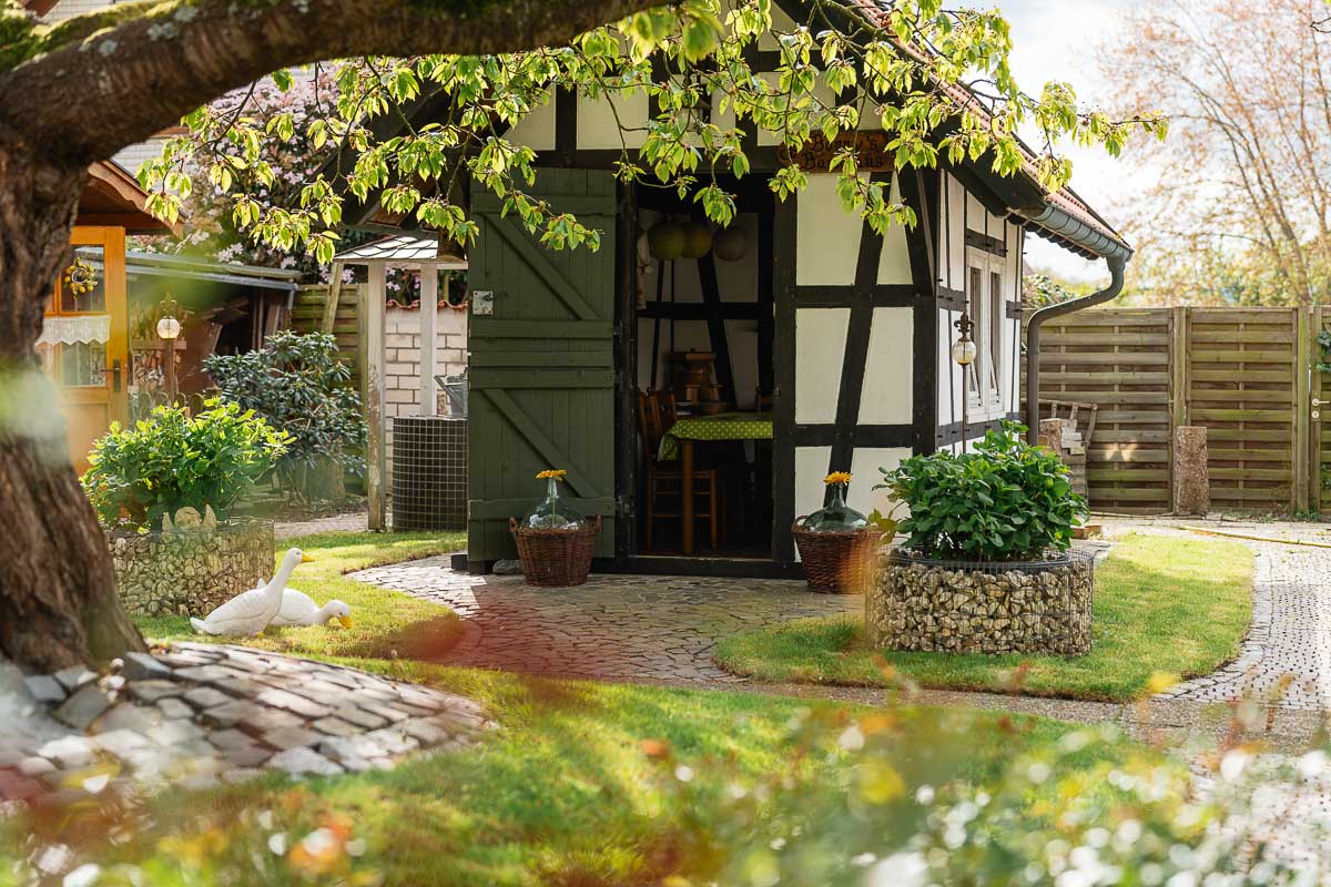 Backhaus aus Fachwerk mit offener grüner Holztür in einem Garten unter einem Blätterdach